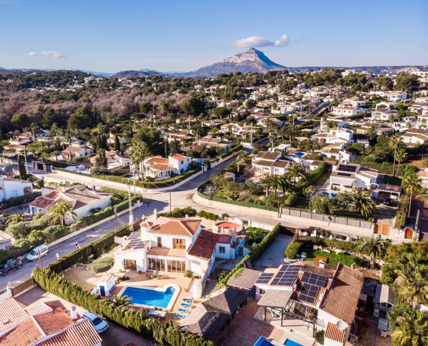 Vista aérea de la propiedad con piscina privada y paneles solares, situada en una zona residencial tranquila con vistas despejadas al monte Montgó.