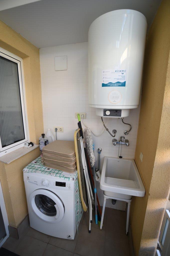 Galería exterior techada equipada con lavadora, termo eléctrico de gran capacidad y un práctico fregadero de servicio para tareas domésticas.