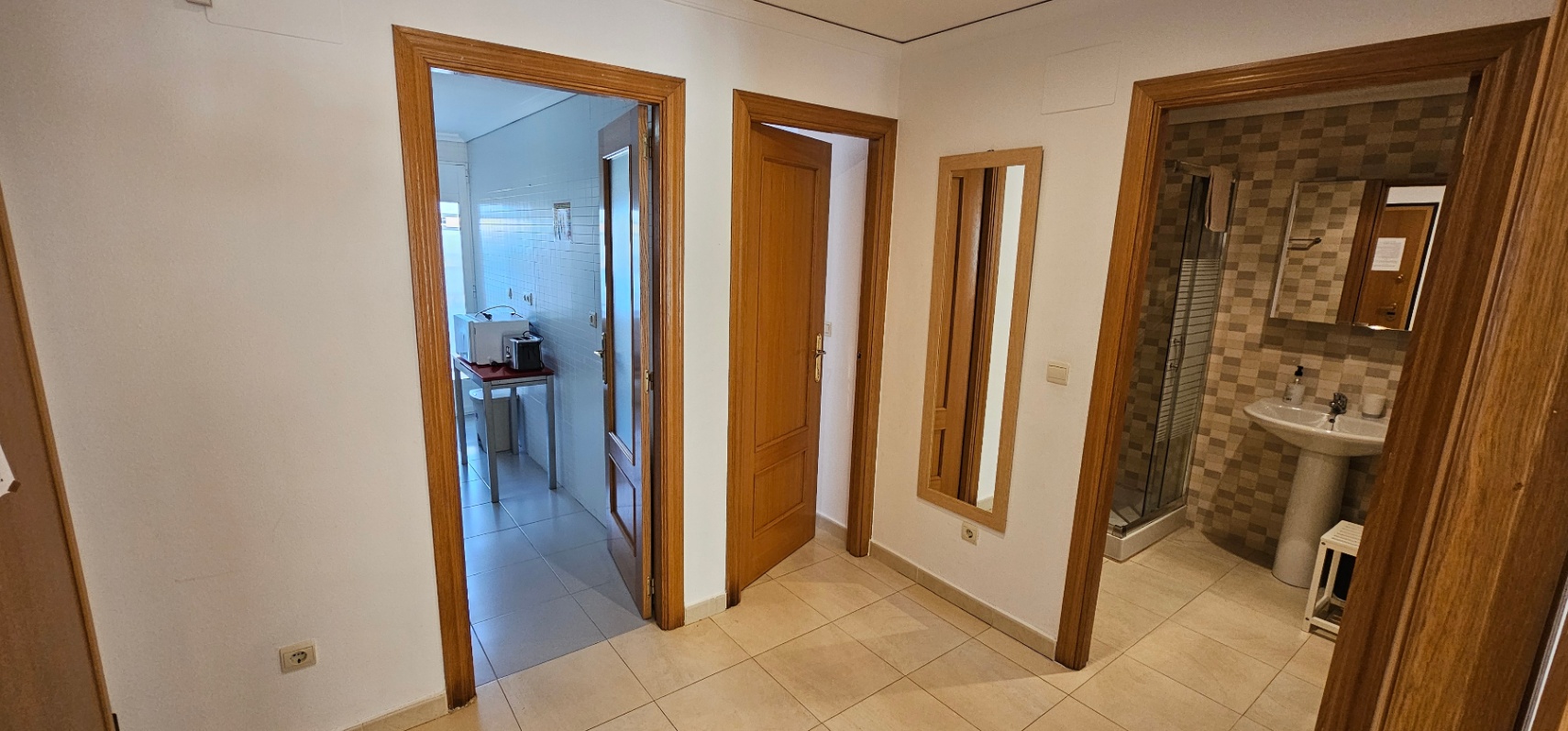 Pasillo distribuidor con suelos cerámicos que conecta la cocina, un dormitorio y un baño completo con ducha y paredes alicatadas.