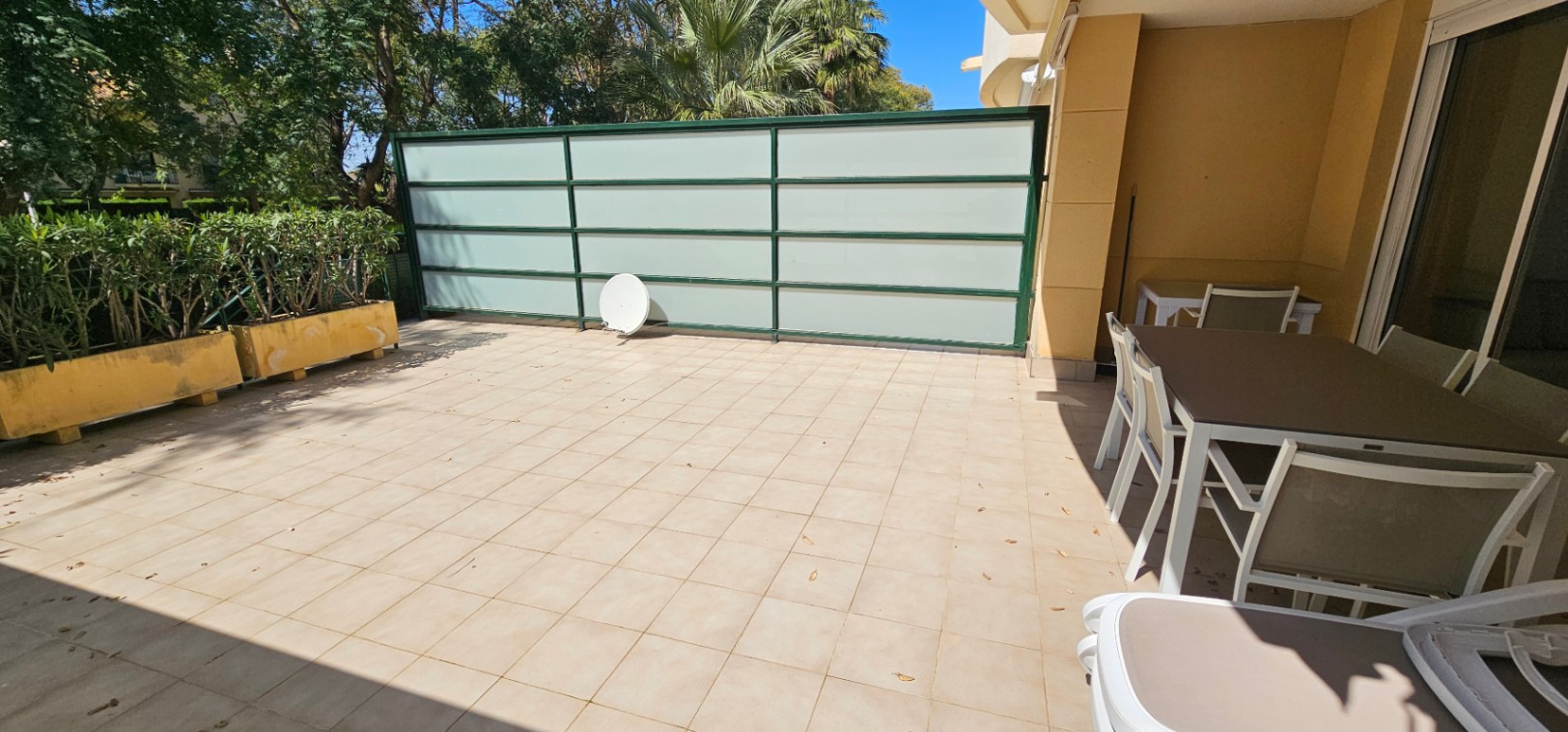Terraza privada con suelo de baldosas cerámicas, zona de comedor exterior bajo porche y panel de cristal traslúcido para mayor privacidad.