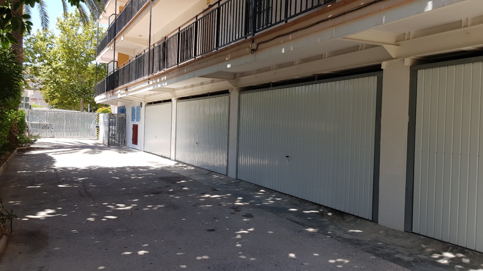 Garajes privados cerrados con puertas metálicas blancas, situados en la planta baja del edificio con acceso directo desde la zona comunitaria pavimentada.