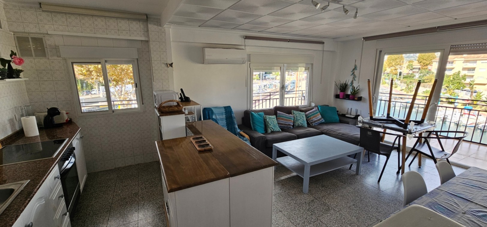 Salón de planta abierta con cocina integrada, barra de madera y acceso directo a la terraza con vistas al canal y la zona náutica.