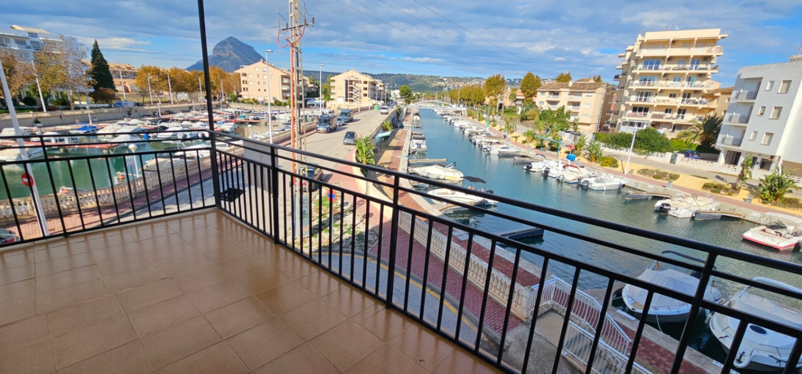 Terraza con suelo cerámico y barandilla negra que ofrece vistas directas al canal de la marina y al emblemático monte Montgó en el horizonte.