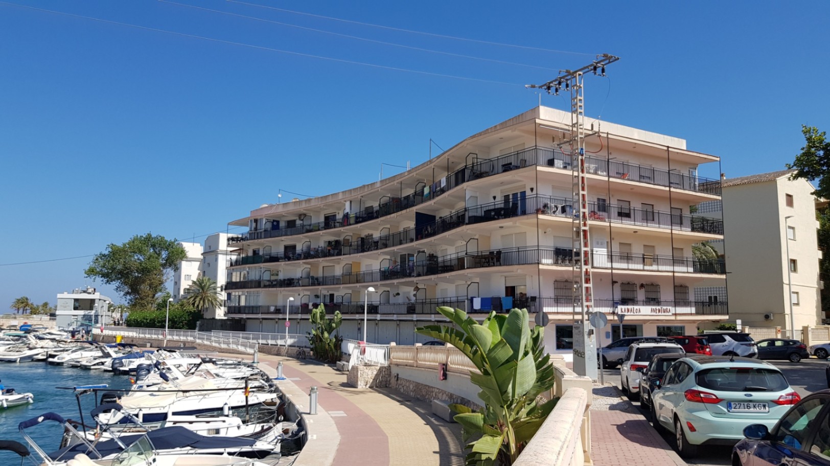 Vista exterior del edificio con balcones curvos y barandillas de forja, situado frente al canal de la marina con embarcaciones recreativas en Jávea.