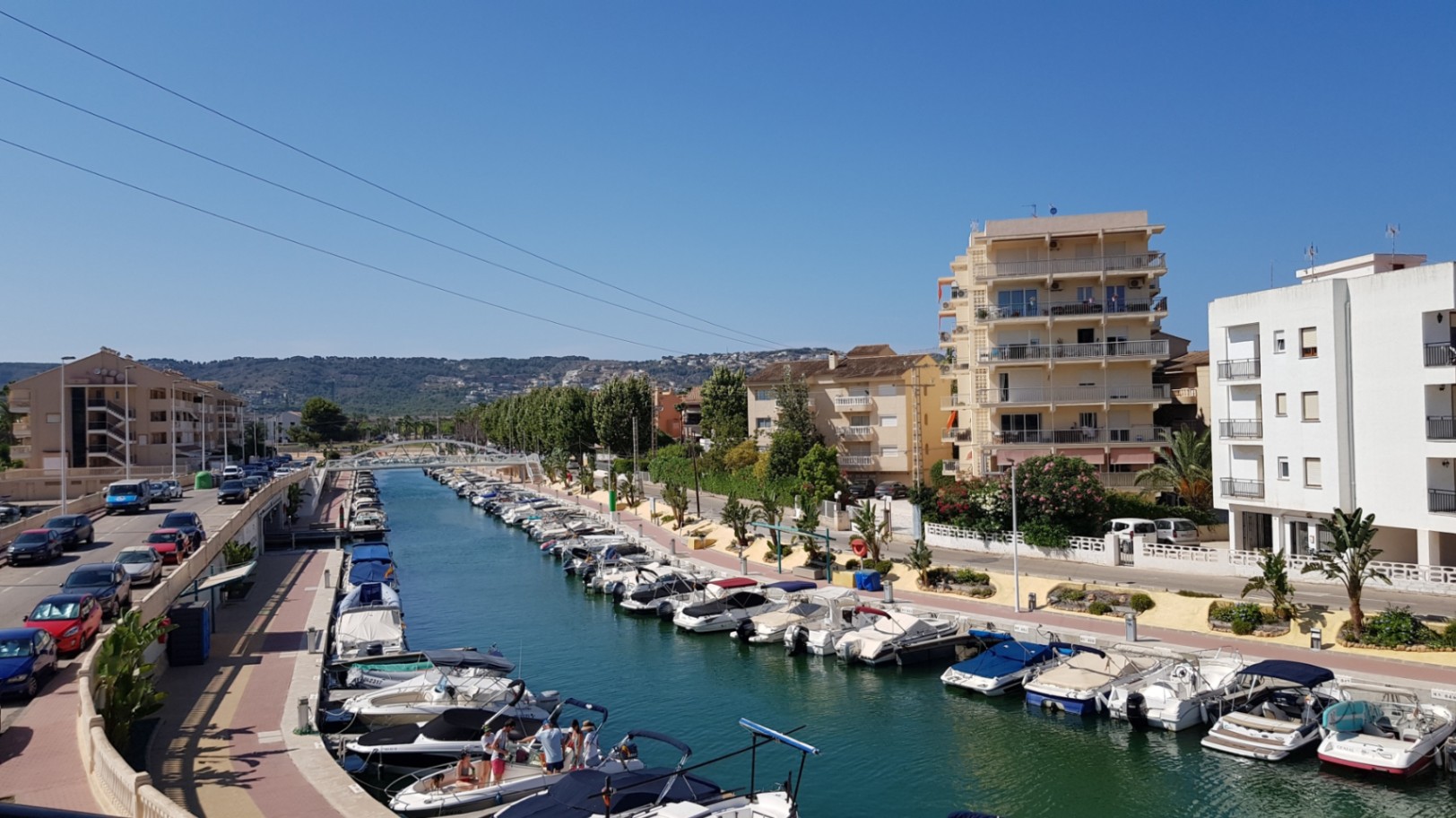 Vistas desde la terraza al canal de la marina de Jávea, con embarcaciones de recreo amarradas y edificios residenciales bajo un cielo despejado.