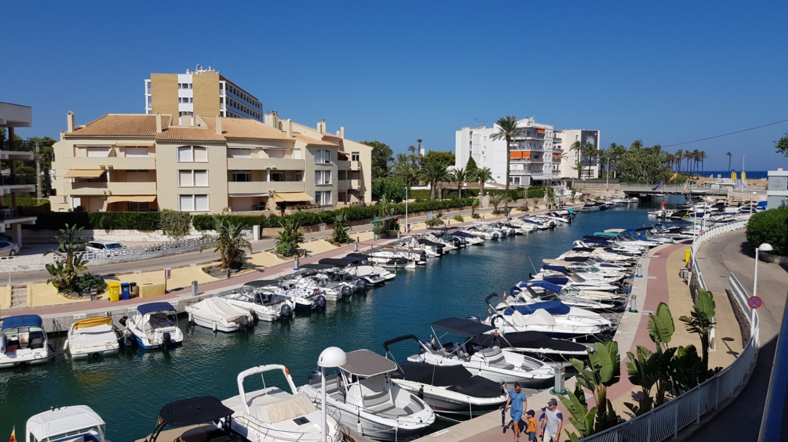 Vistas panorámicas desde la terraza hacia el canal de la marina, con embarcaciones de recreo amarradas y edificios residenciales bajo un cielo despejado en Jávea.