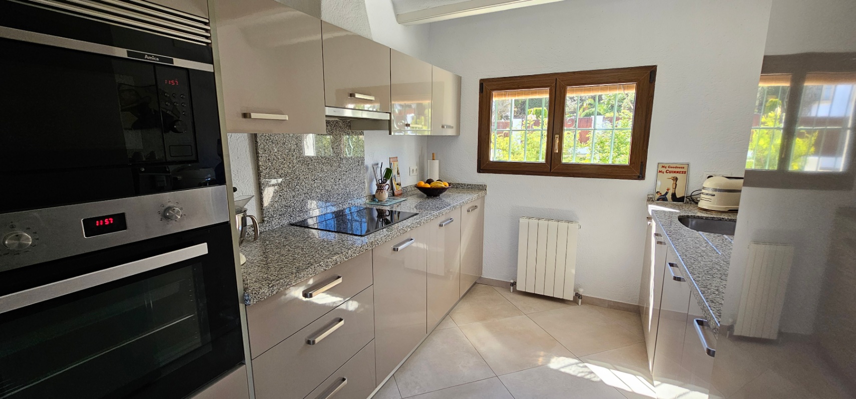 Cocina independiente con mobiliario de alto brillo, encimera de granito y electrodomésticos integrados. Dispone de luz natural a través de una ventana con marco de madera.