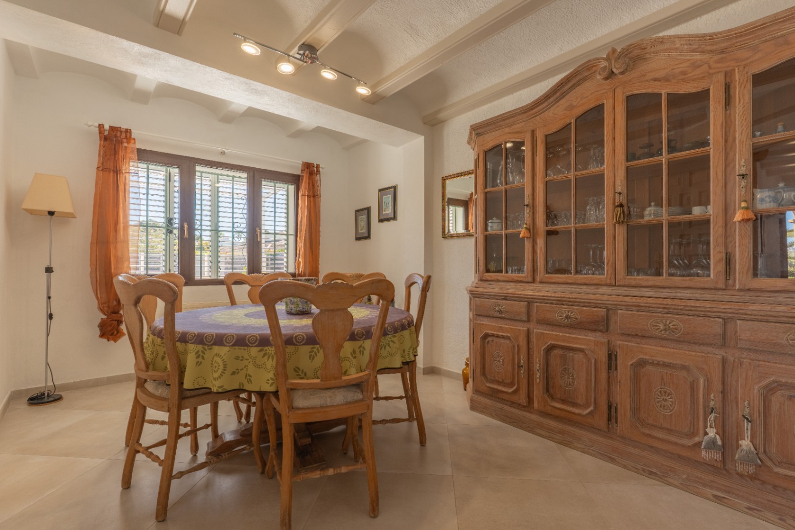 Comedor rústico con techo de vigas vistas, mesa redonda de madera y una gran alacena clásica. La ventana con mallorquinas aporta luz natural al espacio.