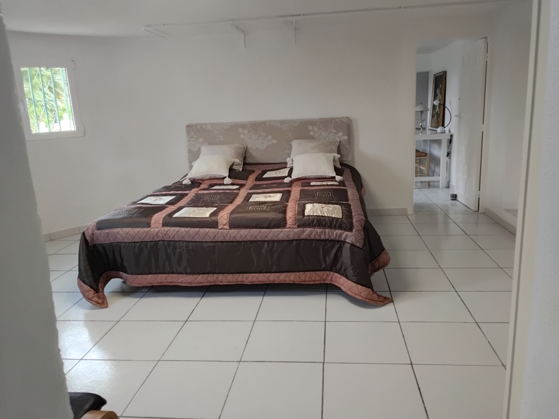 Dormitorio amplio con suelos de baldosa blanca, cama doble con cabecero floral y acceso directo a una estancia contigua ideal como despacho o vestidor.