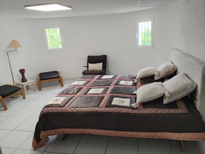 Dormitorio con suelos cerámicos blancos, cama doble y mobiliario auxiliar. Incluye ventanas con rejas de seguridad y una iluminación funcional mediante panel LED de techo.