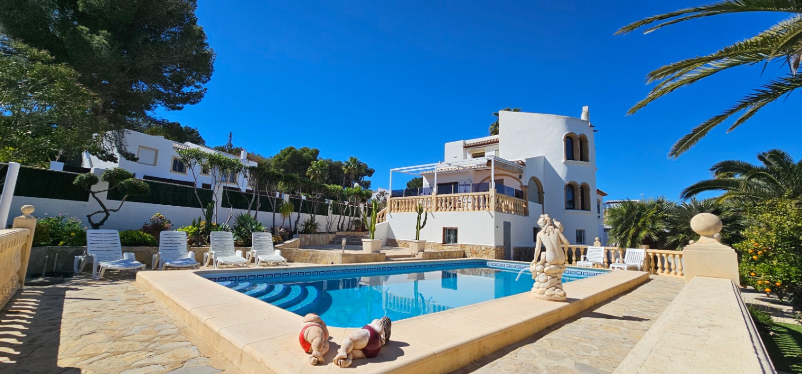 Exterior de la villa con piscina privada rodeada de una amplia terraza de piedra, balaustradas clásicas y vegetación mediterránea autóctona.