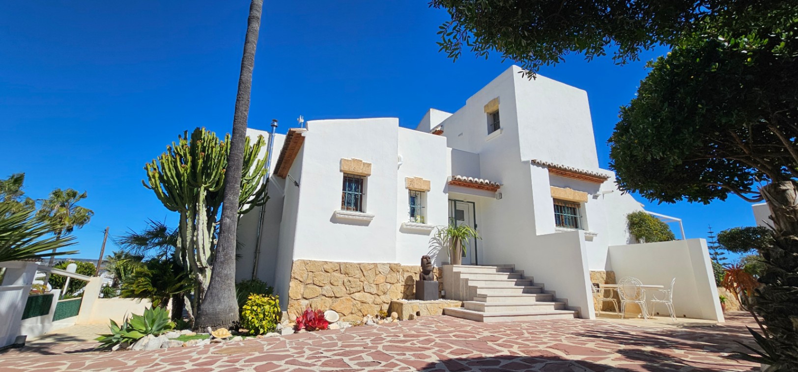 Fachada mediterránea de paredes blancas con zócalo de piedra natural, ventanas con dinteles de tosca y acceso principal mediante escalinata de mármol.