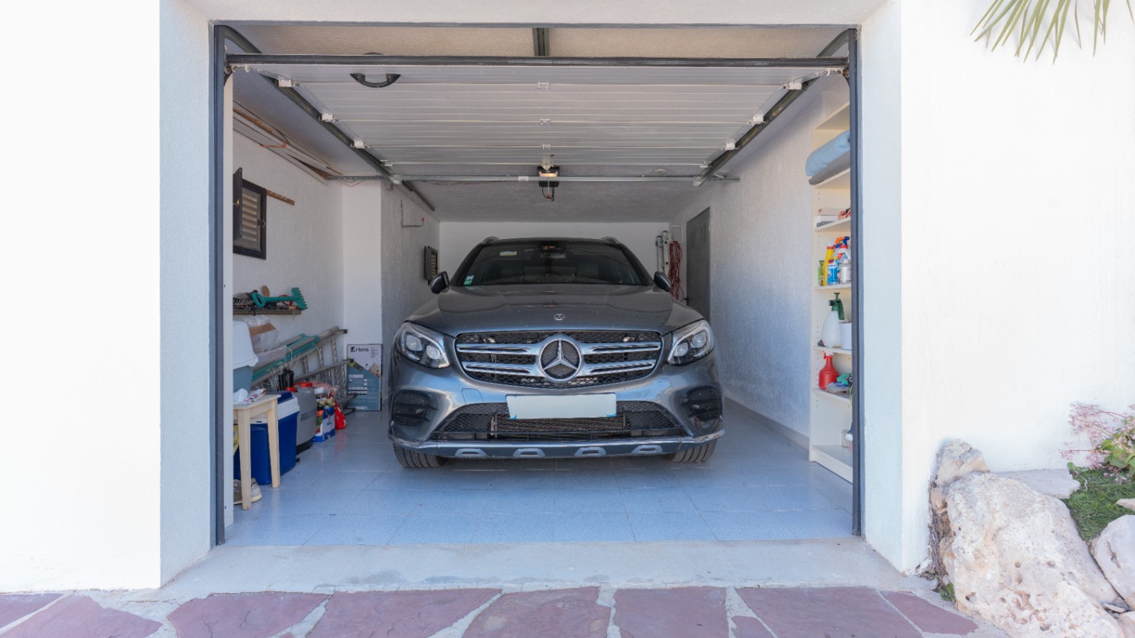 Garaje privado con suelo cerámico, estanterías integradas y puerta seccional automática, ofreciendo un amplio espacio de almacenamiento y protección para vehículos.