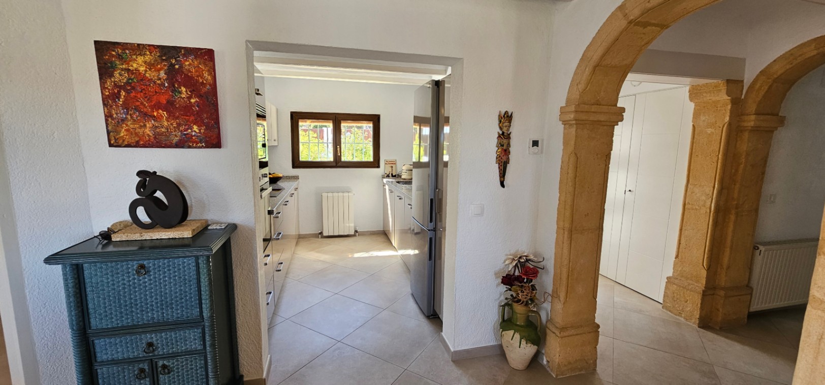 Recibidor con arcos tradicionales de piedra tosca que conecta con una cocina independiente equipada y luminosa con calefacción central.