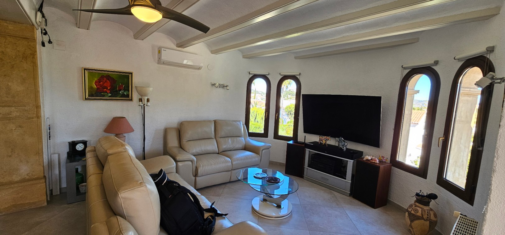 Salón con sofás de cuero, techo de vigas vistas y aire acondicionado. Las ventanas de arco inundan el espacio de luz natural y ofrecen vistas al jardín.