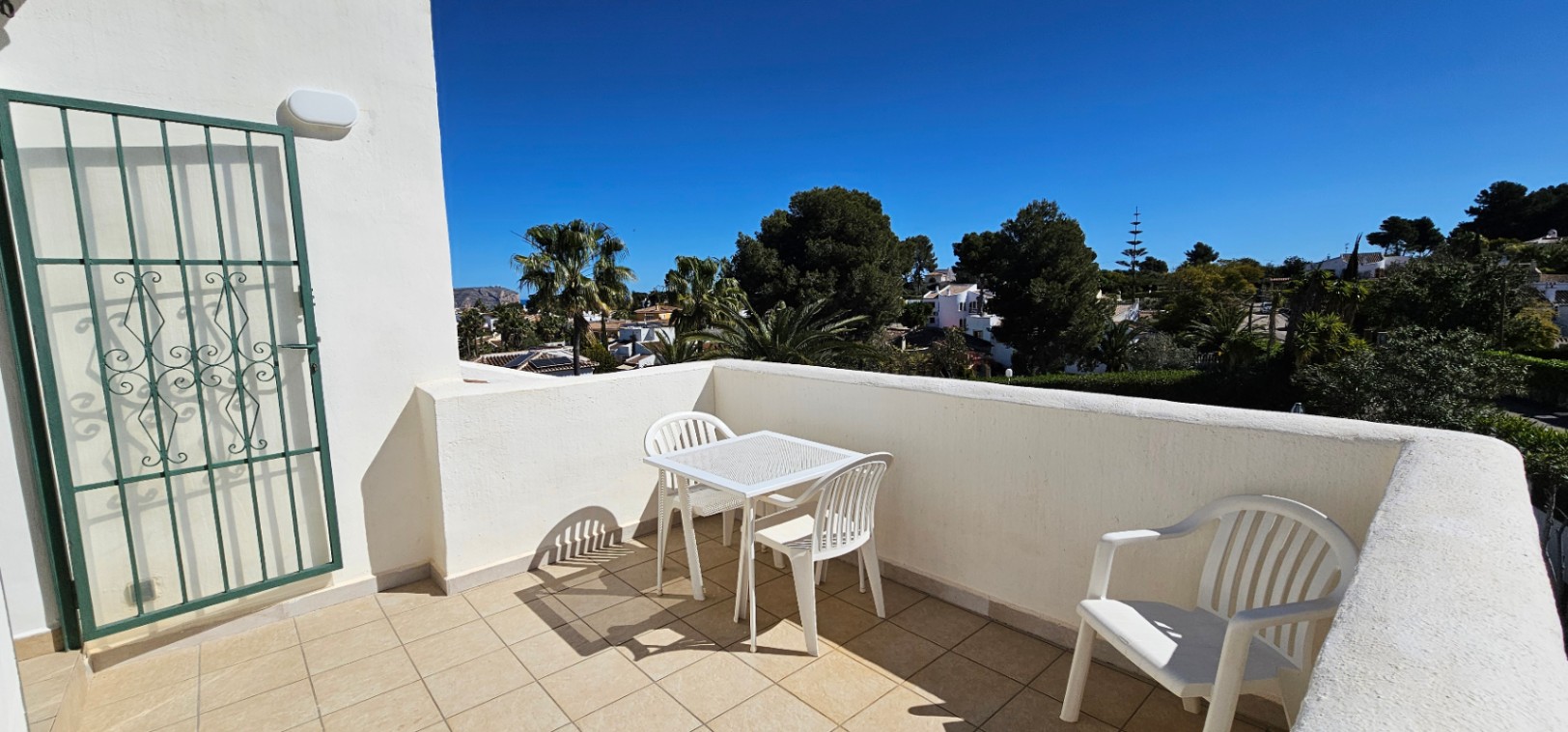 Terraza abierta en planta superior con suelo cerámico, mobiliario de exterior blanco y vistas despejadas al entorno arbolado de Pinosol bajo el sol mediterráneo.