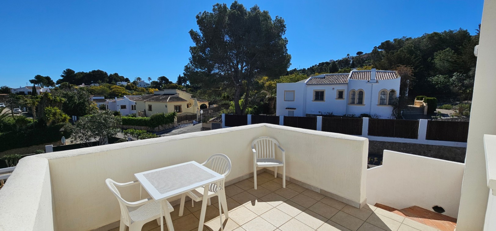 Terraza abierta en planta superior con suelo cerámico, mobiliario de exterior blanco y vistas despejadas al entorno residencial de Pinosol bajo el sol mediterráneo.