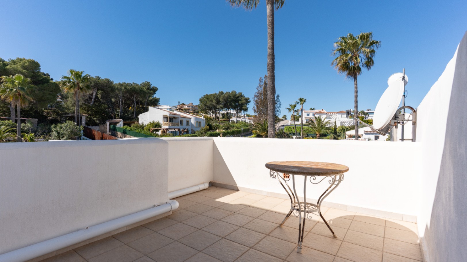 Terraza superior con suelo cerámico y vistas despejadas a la urbanización Pinosol, equipada con mesa auxiliar de forja y antena parabólica.