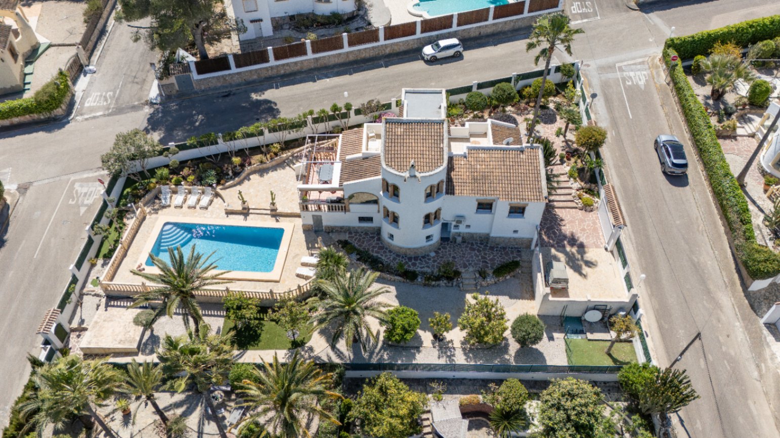 Vista aérea de la propiedad en parcela de esquina, destacando la piscina rectangular, la torre circular y el jardín mediterráneo con palmeras.
