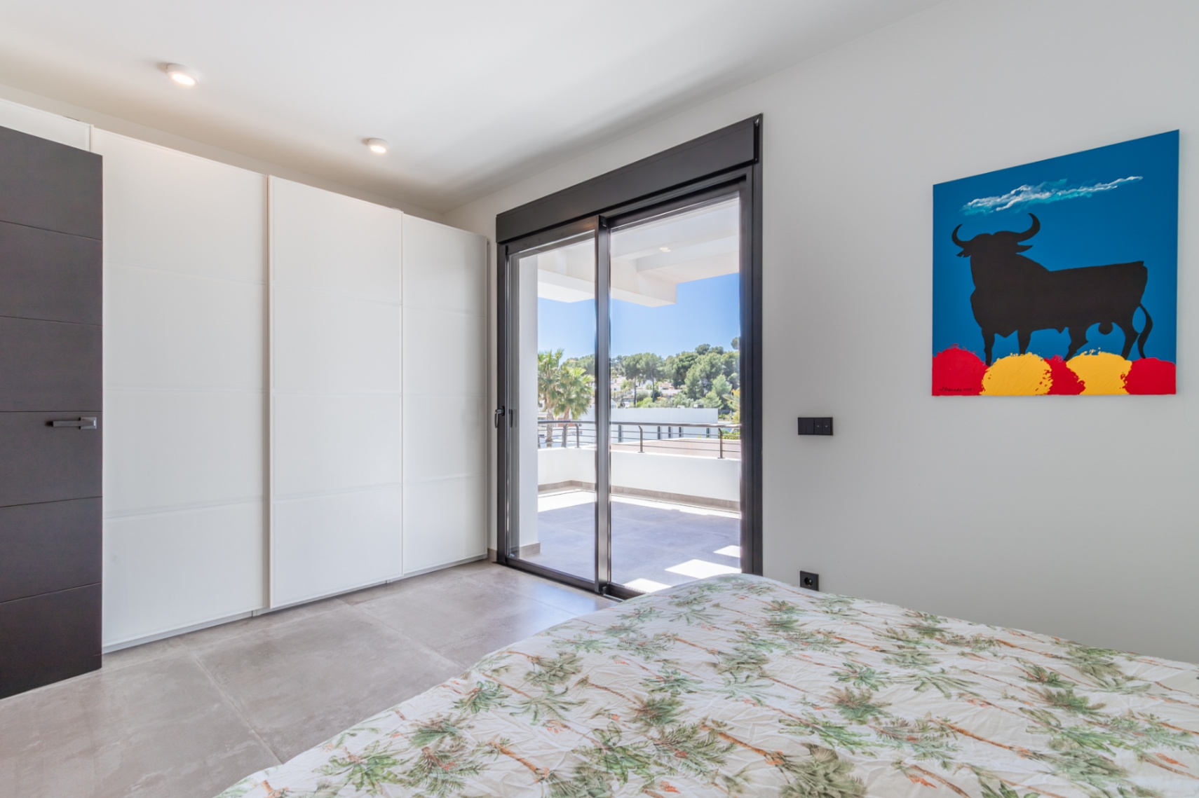Dormitorio con armarios empotrados blancos, suelos de gres y acceso directo a una terraza privada a través de grandes ventanales correderos.