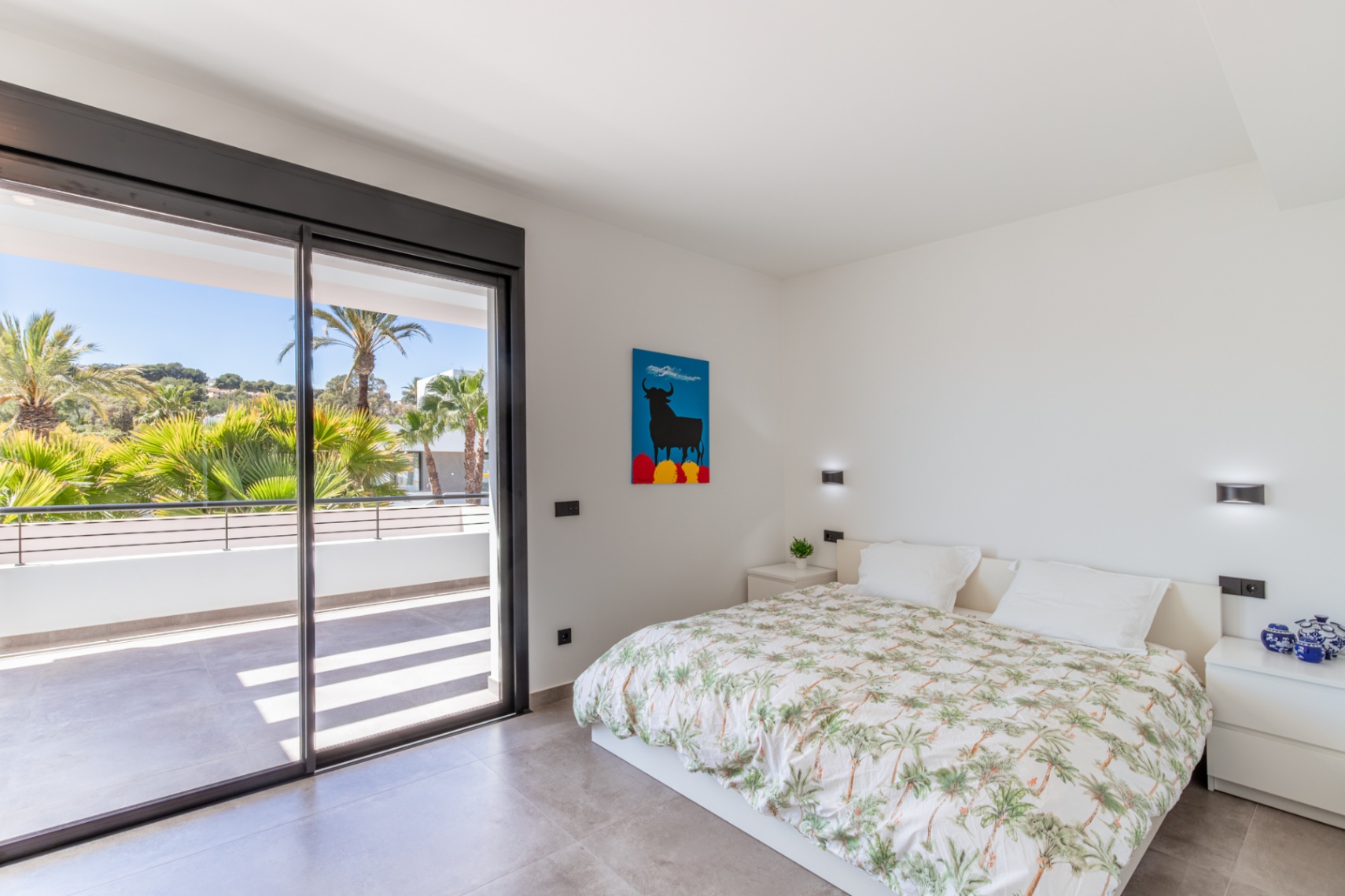 Dormitorio luminoso con acceso directo a una terraza privada mediante grandes ventanales correderos. Suelo de gres gris y paredes blancas con iluminación integrada.