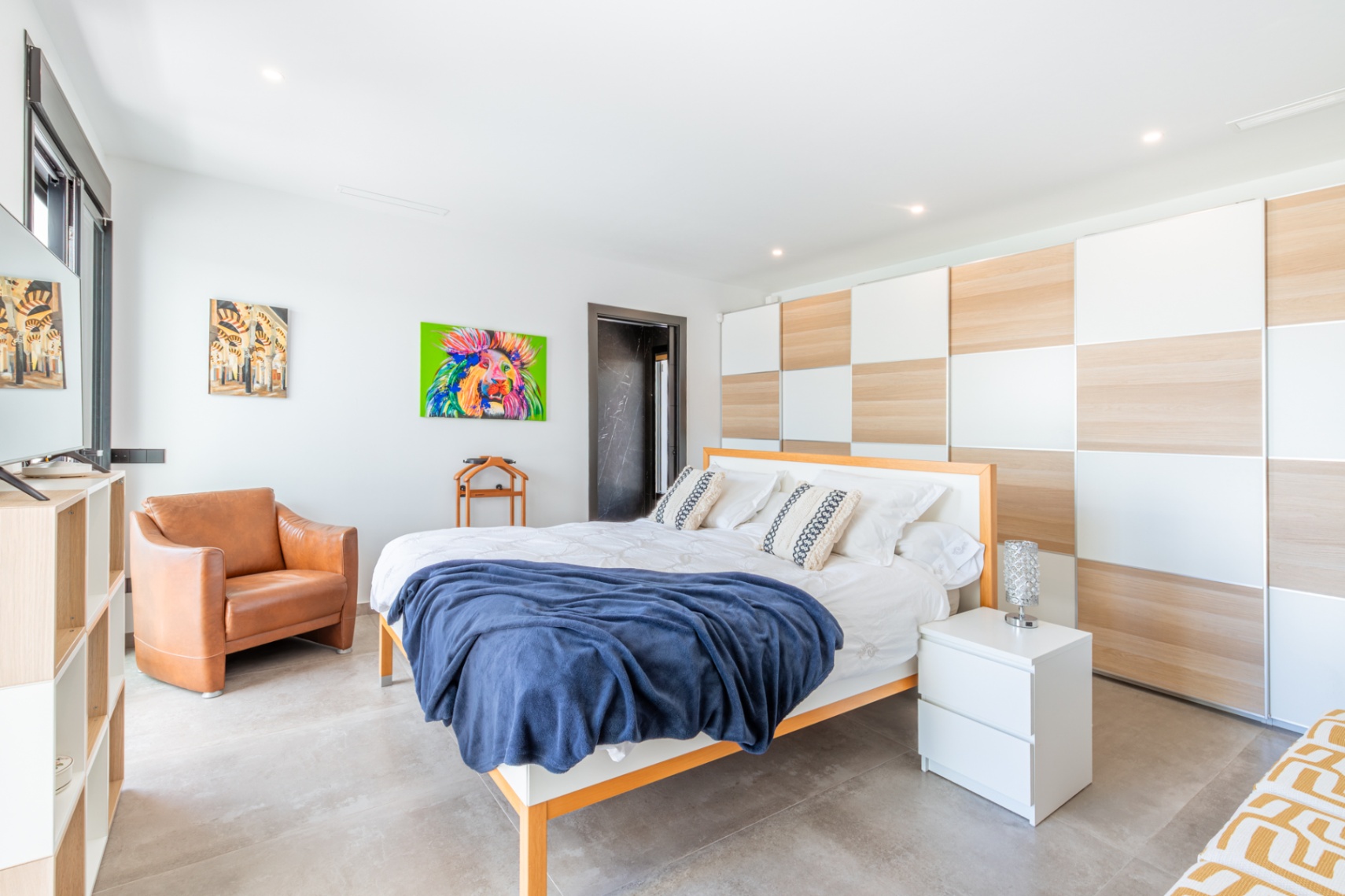 Dormitorio luminoso con armarios empotrados de diseño ajedrezado en madera y blanco, suelos de gres gris y mobiliario contemporáneo que incluye un sillón de cuero.