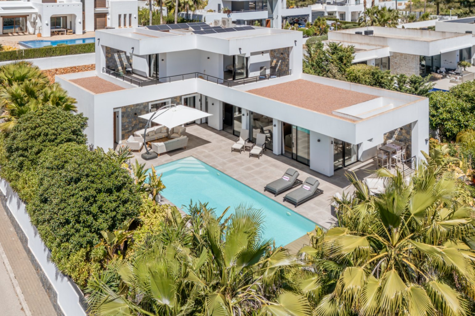 Vista aérea de la villa moderna con piscina, paneles solares en el tejado y amplias terrazas rodeadas de vegetación mediterránea privada.