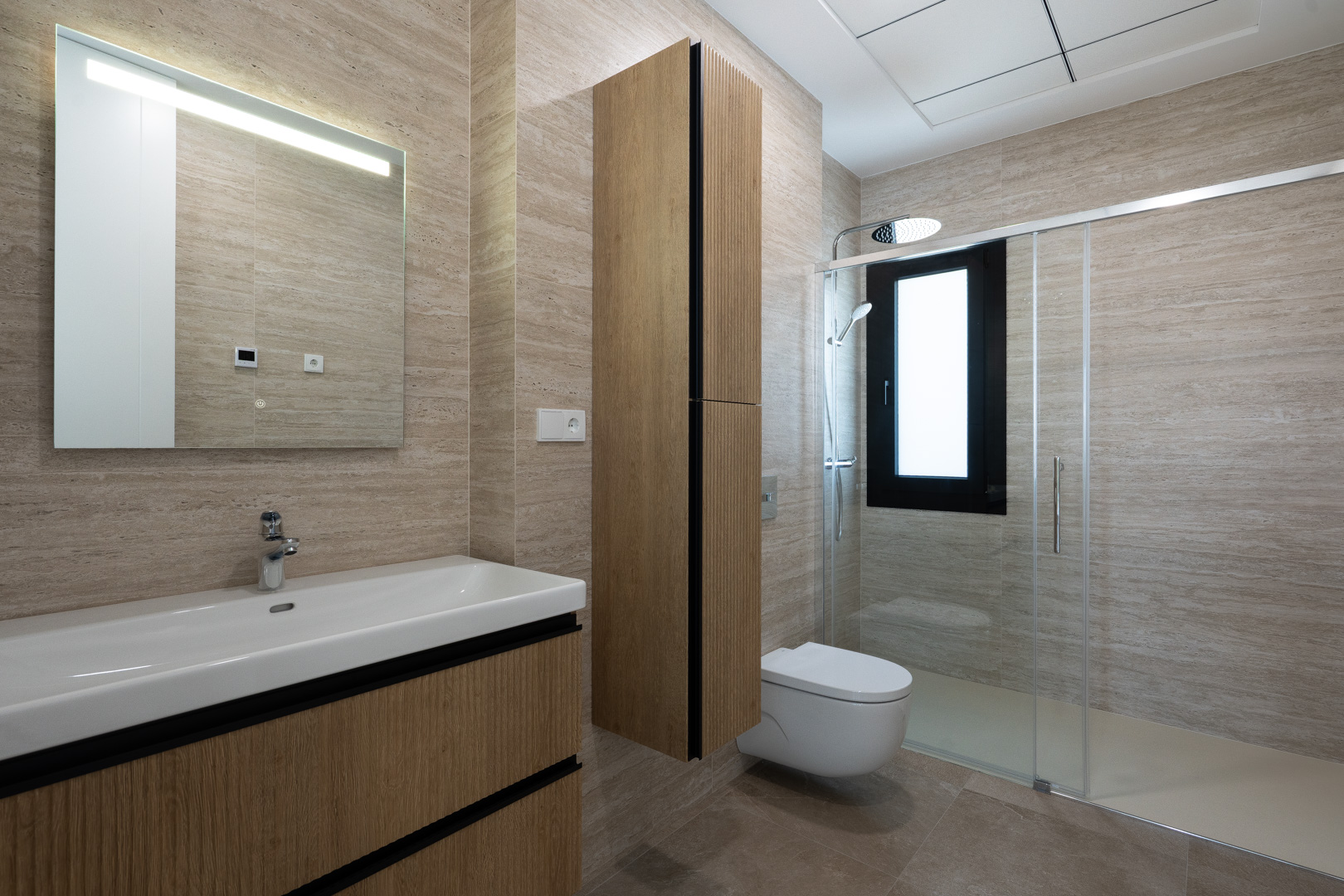 Baño moderno con revestimiento porcelánico texturizado, mueble de lavabo flotante en madera, inodoro suspendido y ducha italiana con mampara de cristal.