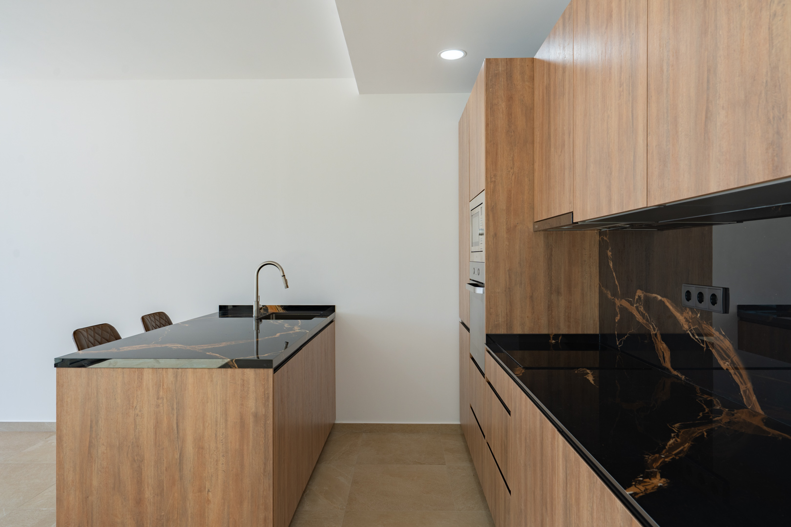 Cocina de diseño con mobiliario de acabado madera, encimeras de piedra oscura veteada e isla central con fregadero integrado y grifería minimalista.