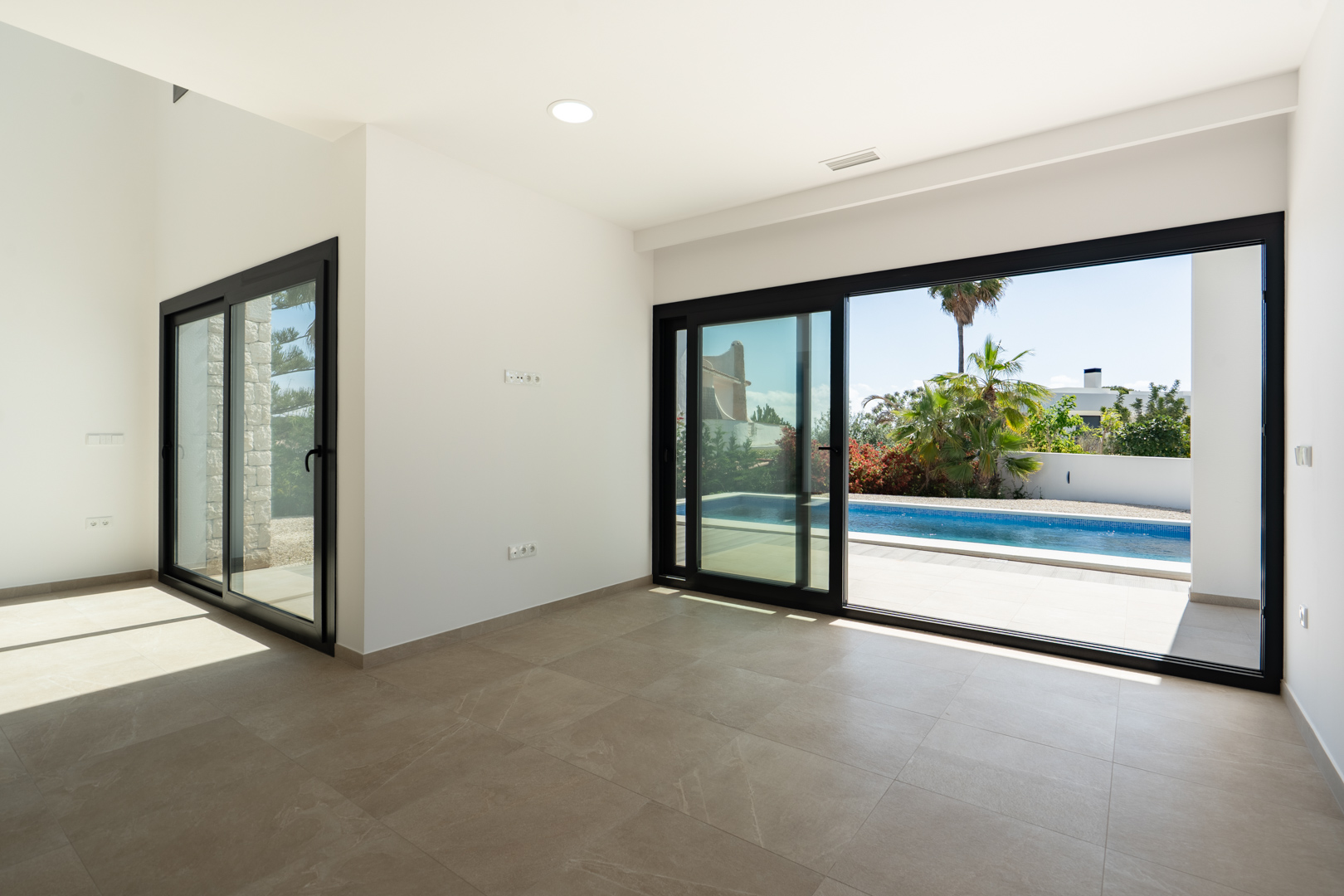 Salón luminoso con suelos porcelánicos y amplios ventanales correderos de perfilería negra que conectan directamente con la terraza y la piscina privada.