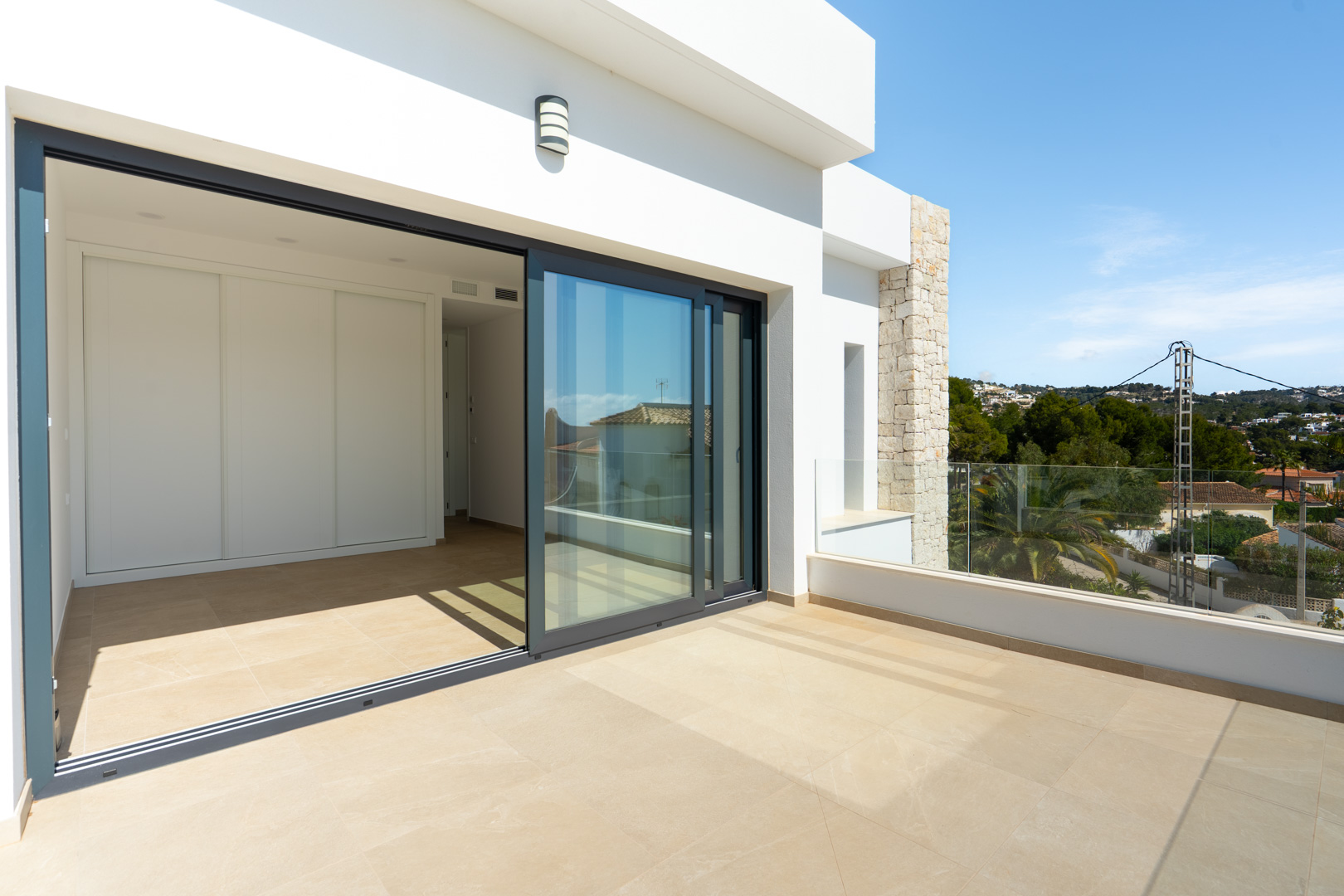 Terraza en planta superior con suelos porcelánicos, barandilla de cristal y acceso directo al dormitorio mediante amplios ventanales correderos.