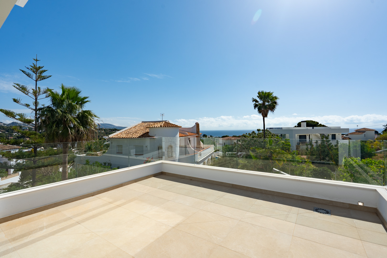 Terraza superior con suelo porcelánico de gran formato y barandillas de cristal que ofrecen vistas despejadas al mar Mediterráneo y al entorno residencial de Benissa.