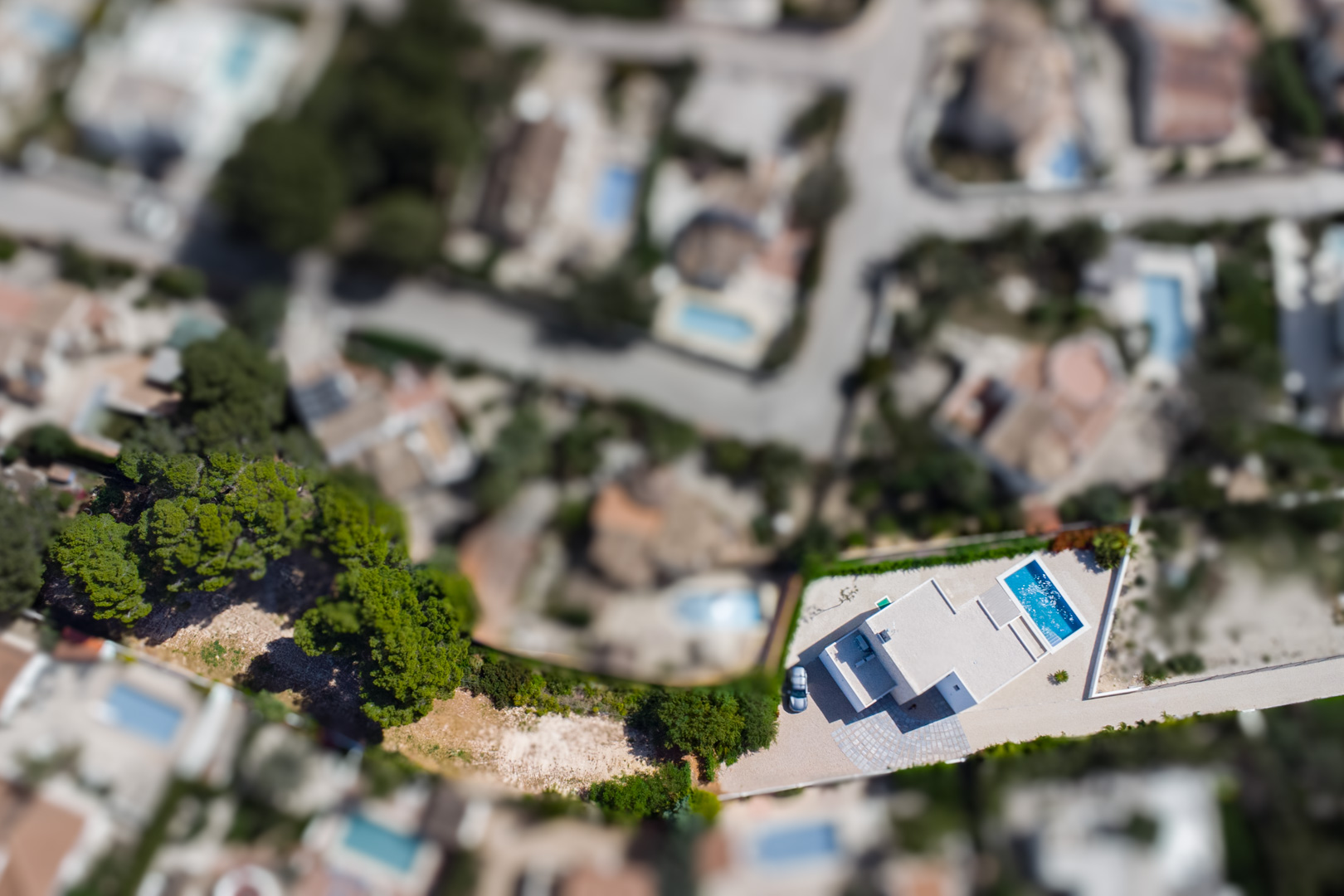 Vista aérea cenital de la villa moderna sobre su amplia parcela llana, destacando la piscina rectangular azul y la distribución funcional del exterior en La Fustera.