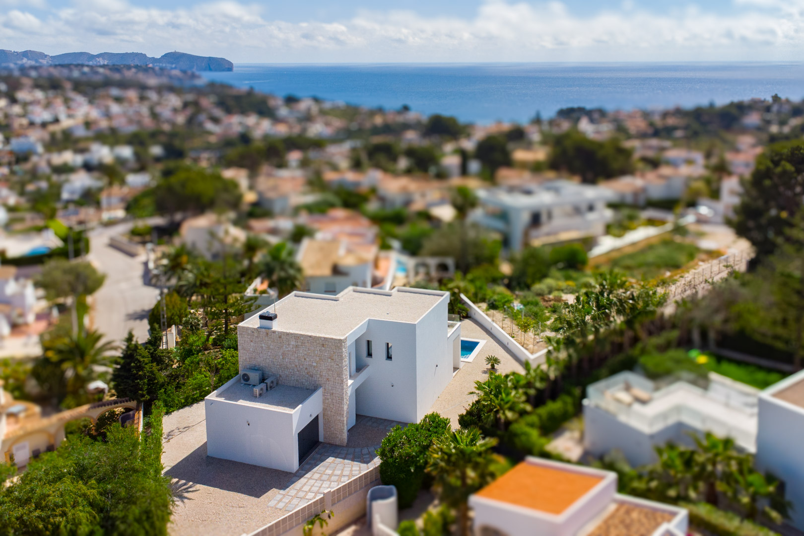 Vista aérea de la villa moderna con fachada de piedra natural y líneas blancas, situada en una zona residencial con vistas panorámicas al mar Mediterráneo.
