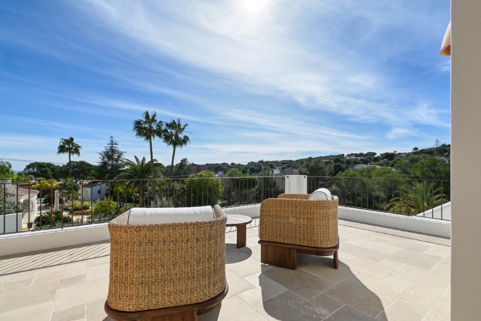 Terraza superior con suelo de piedra natural y mobiliario de mimbre, ofreciendo vistas despejadas al entorno verde y palmeras de Moraira.