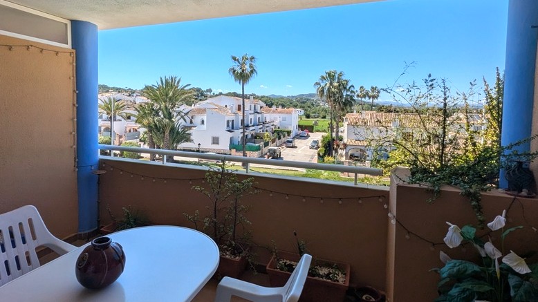 Terraza cubierta con zona de comedor y vistas despejadas a villas mediterráneas, palmeras y el macizo del Montgó al fondo.
