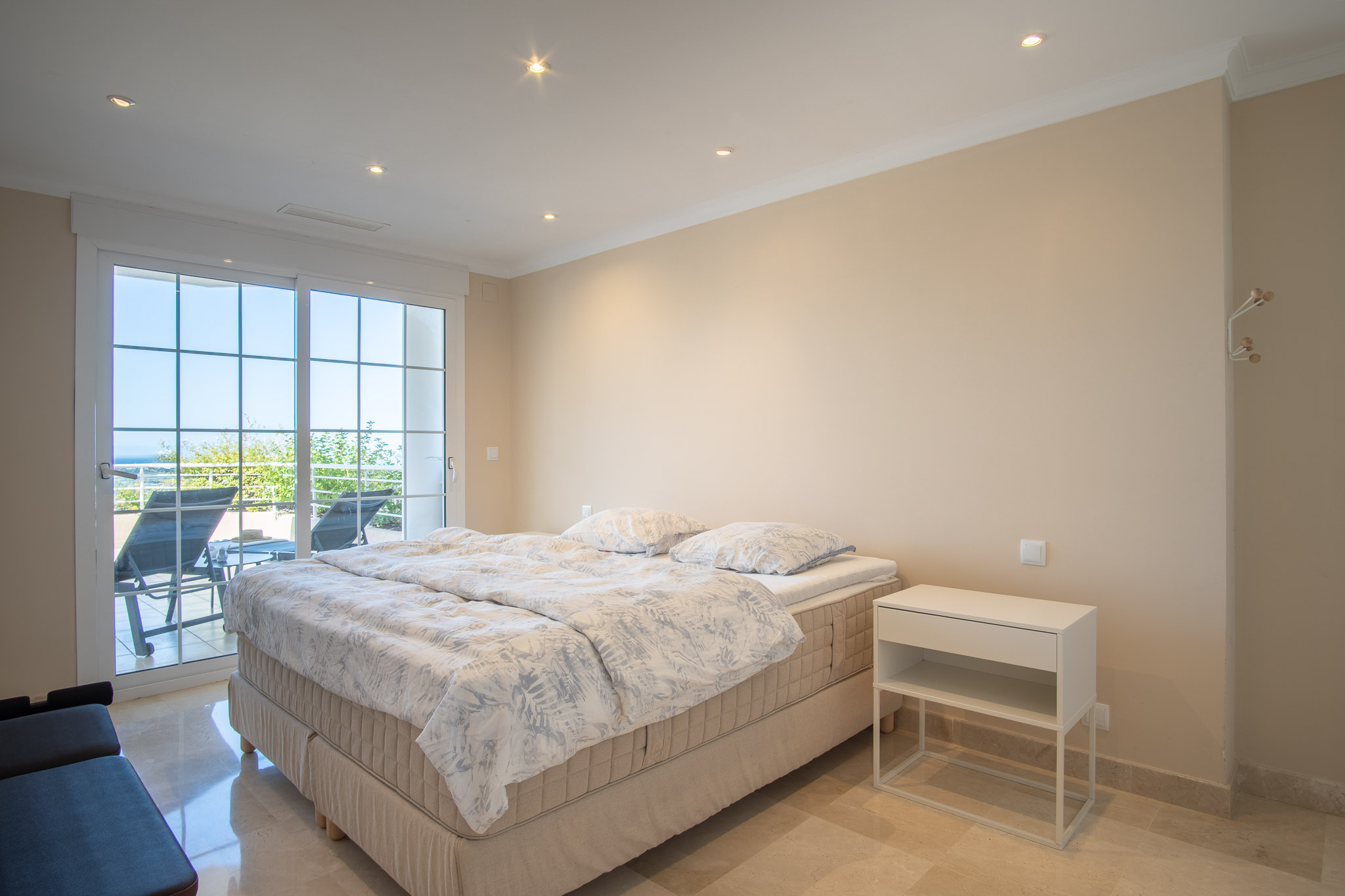Dormitorio con suelos de mármol y acceso directo a la terraza. La estancia cuenta con iluminación empotrada y ventanales que integran el exterior con la zona de descanso.