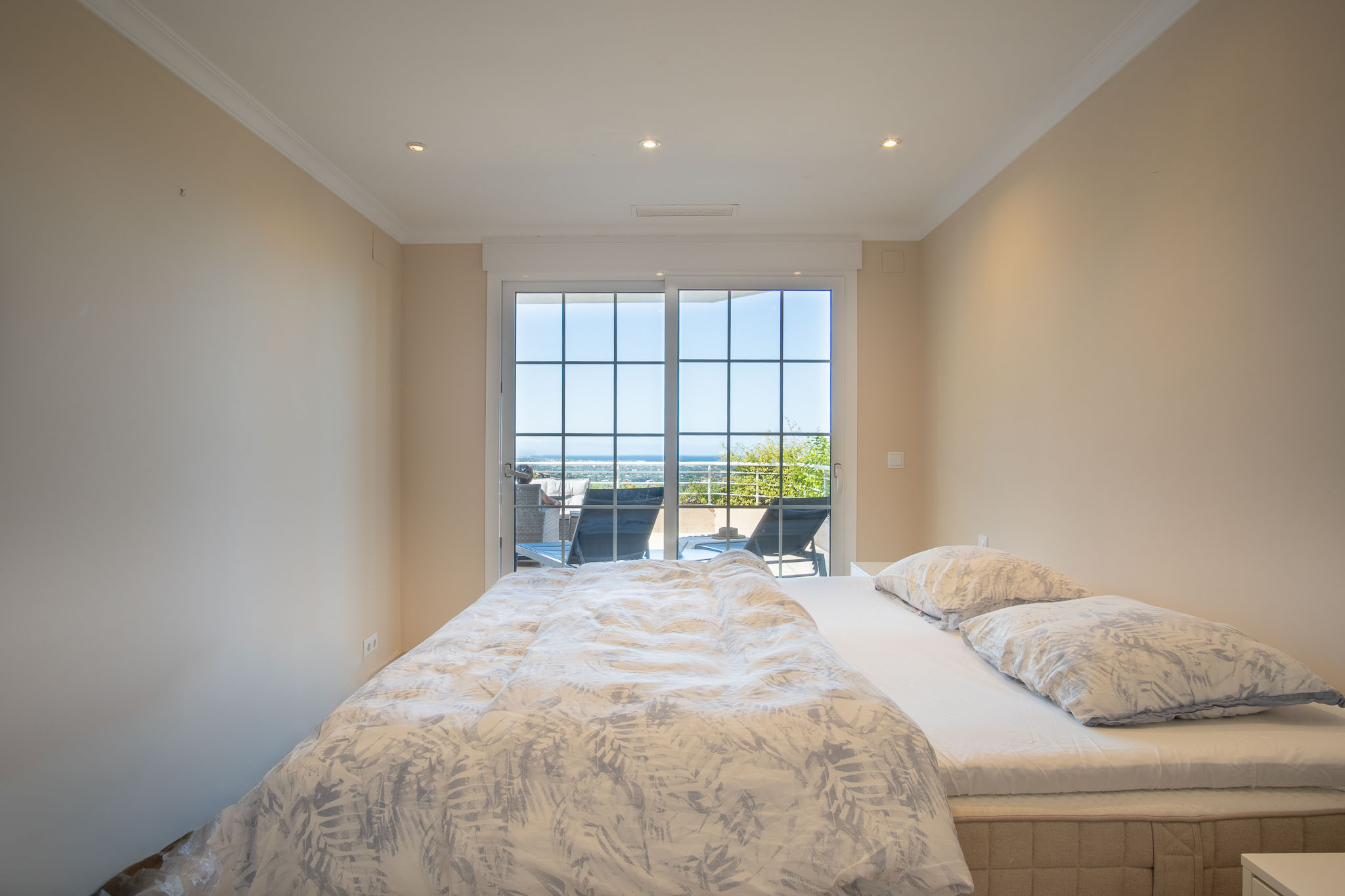 Dormitorio doble con acceso directo a la terraza mediante ventanales de cuadrícula, ofreciendo vistas despejadas al mar y abundante luz natural.