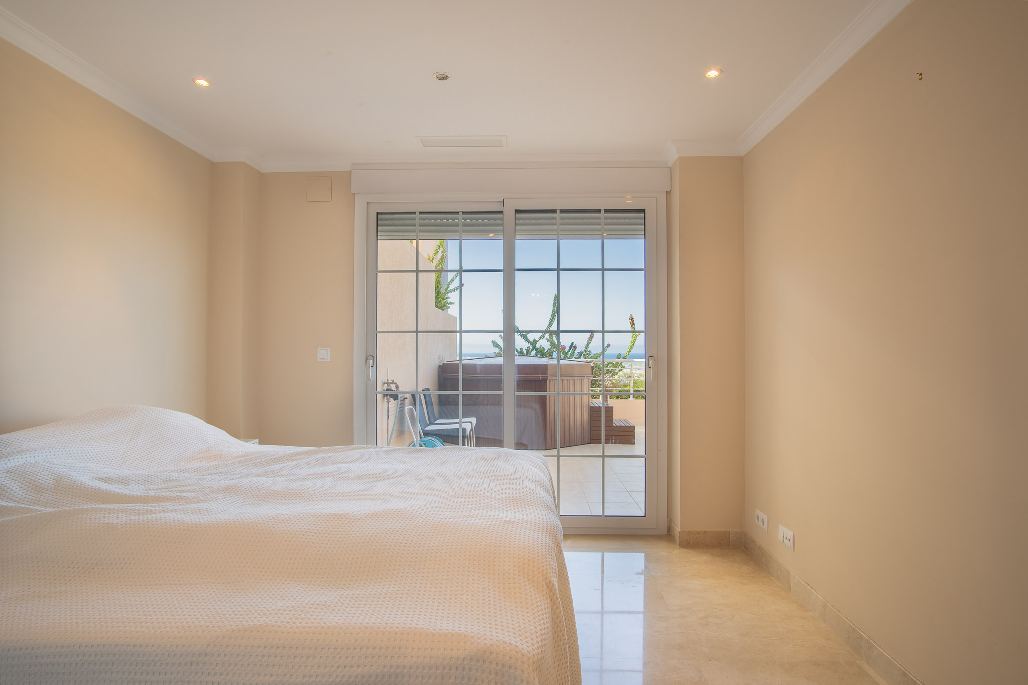 Dormitorio luminoso con suelos de mármol y acceso directo a la terraza privada con jacuzzi y vistas al mar.