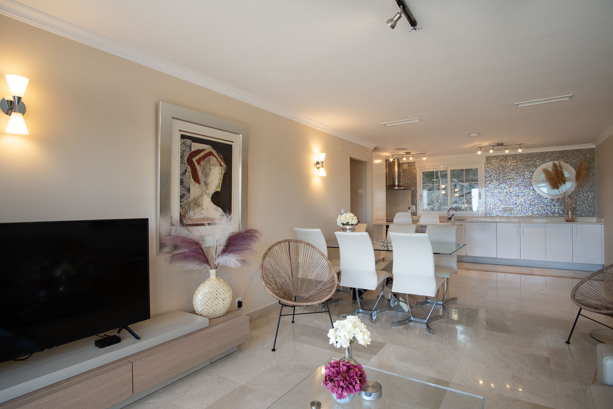 Salón-comedor de planta abierta con suelos de mármol pulido, mobiliario moderno y una cocina integrada con un distintivo salpicadero de mosaico iridiscente.