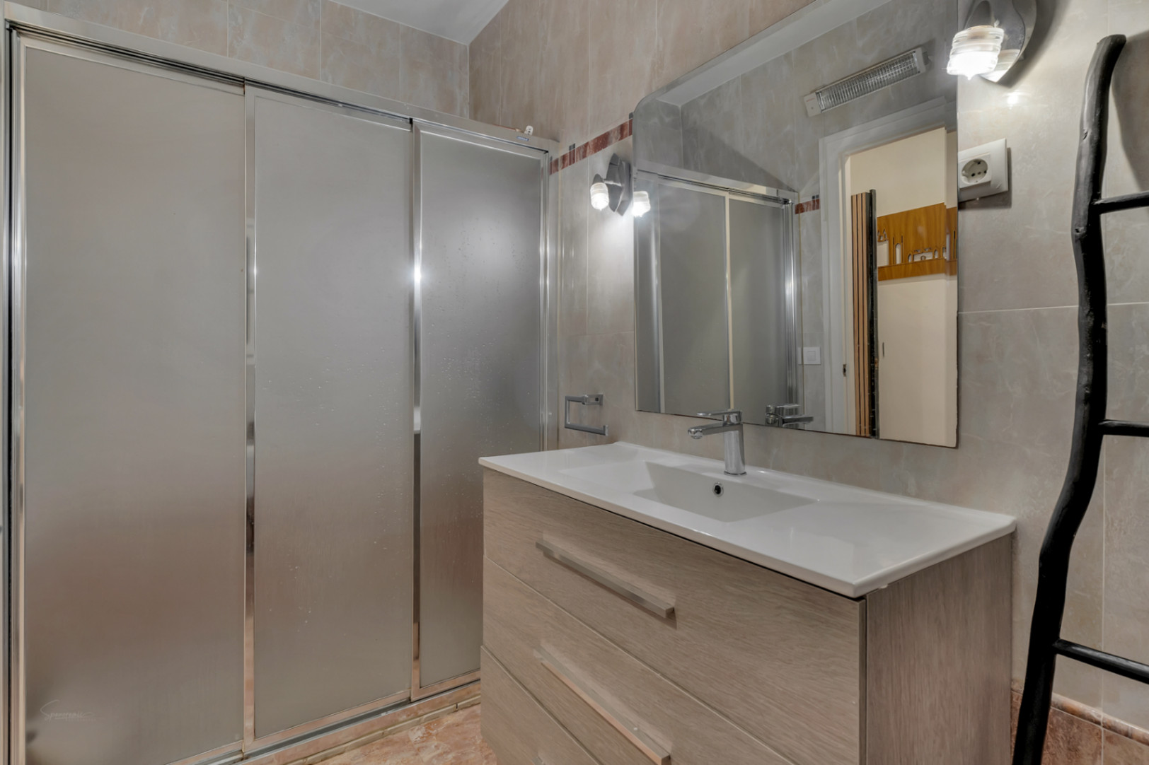 Detalle de baño con lavabo encastrado en mueble de madera clara y ducha con mampara corredera.