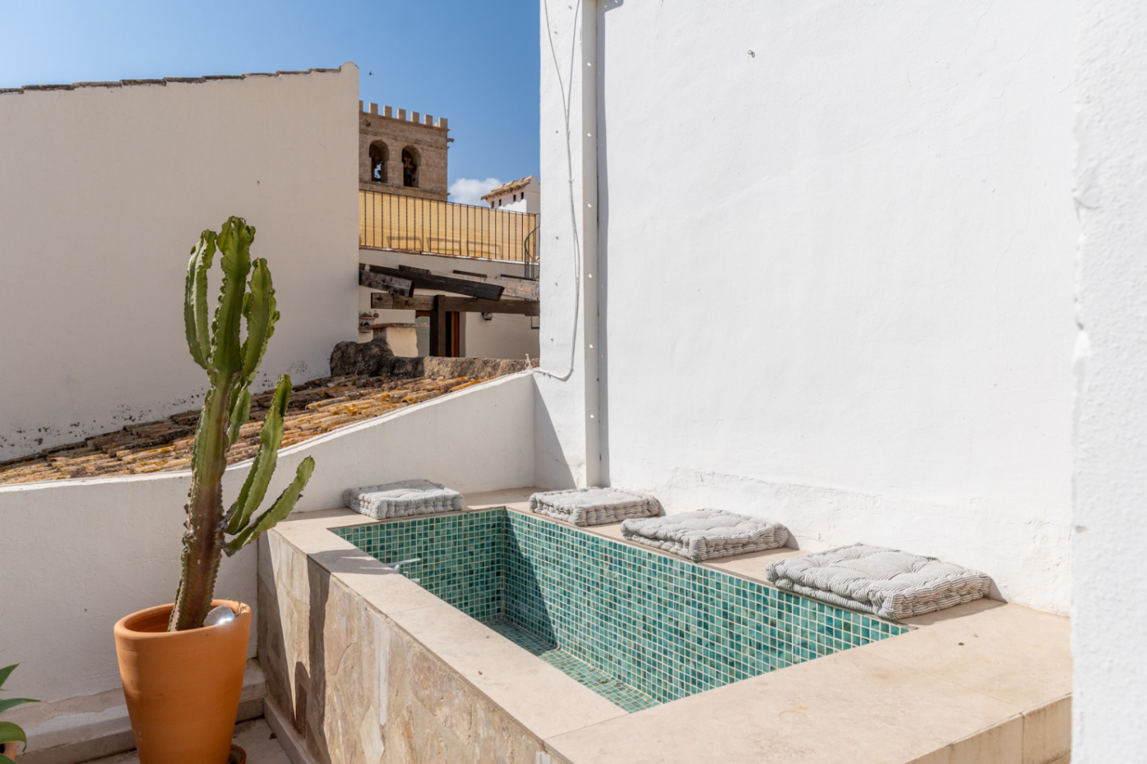 Detalle de la terraza con jacuzzi de mosaico turquesa y cactus en maceta, con vistas al casco antiguo.