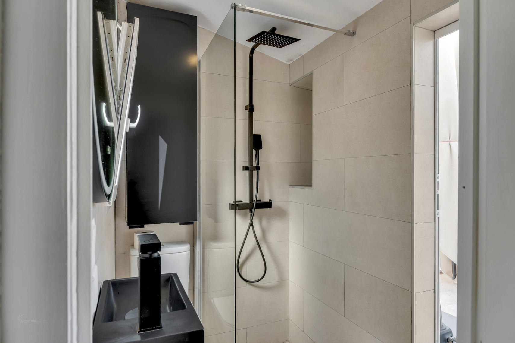 Detalle del baño moderno con ducha de efecto lluvia negra, lavabo negro y azulejos color crema.