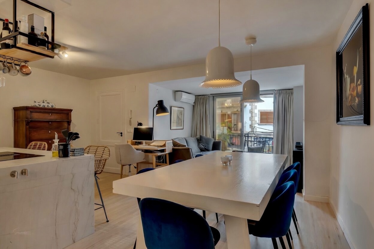 Detalle del salón-comedor con mesa blanca, sillas de terciopelo azul y acceso a la terraza.