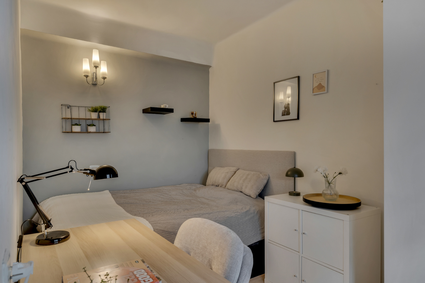 Dormitorio luminoso con escritorio de madera clara y estanterías decorativas en la pared.