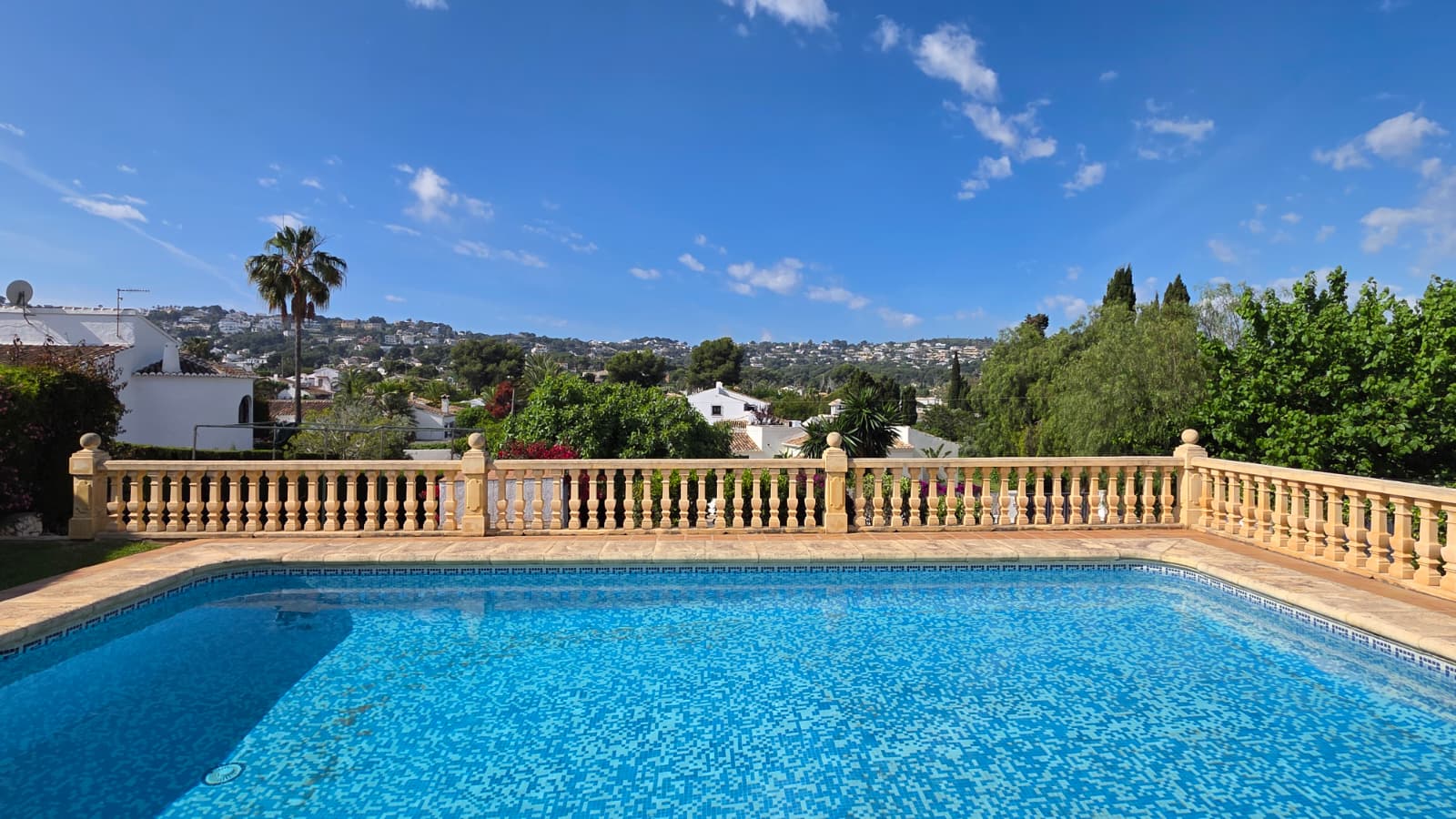 Piscina exterior con mosaico azul y balaustrada de piedra tradicional, ofreciendo vistas despejadas a las colinas y zonas residenciales de El Tosalet, Jávea.