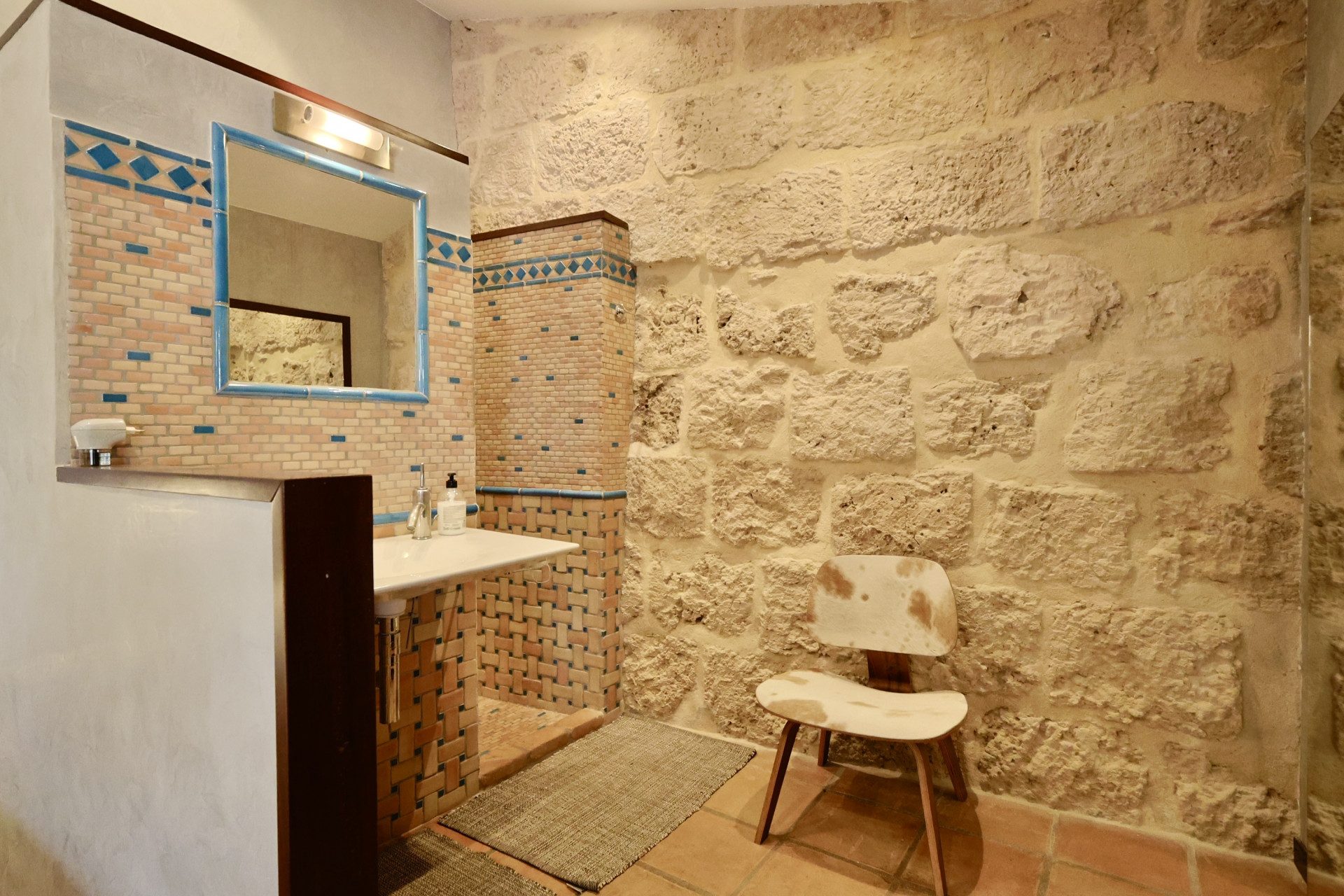 Detalle de baño con pared de piedra vista y lavabo con azulejos decorativos.