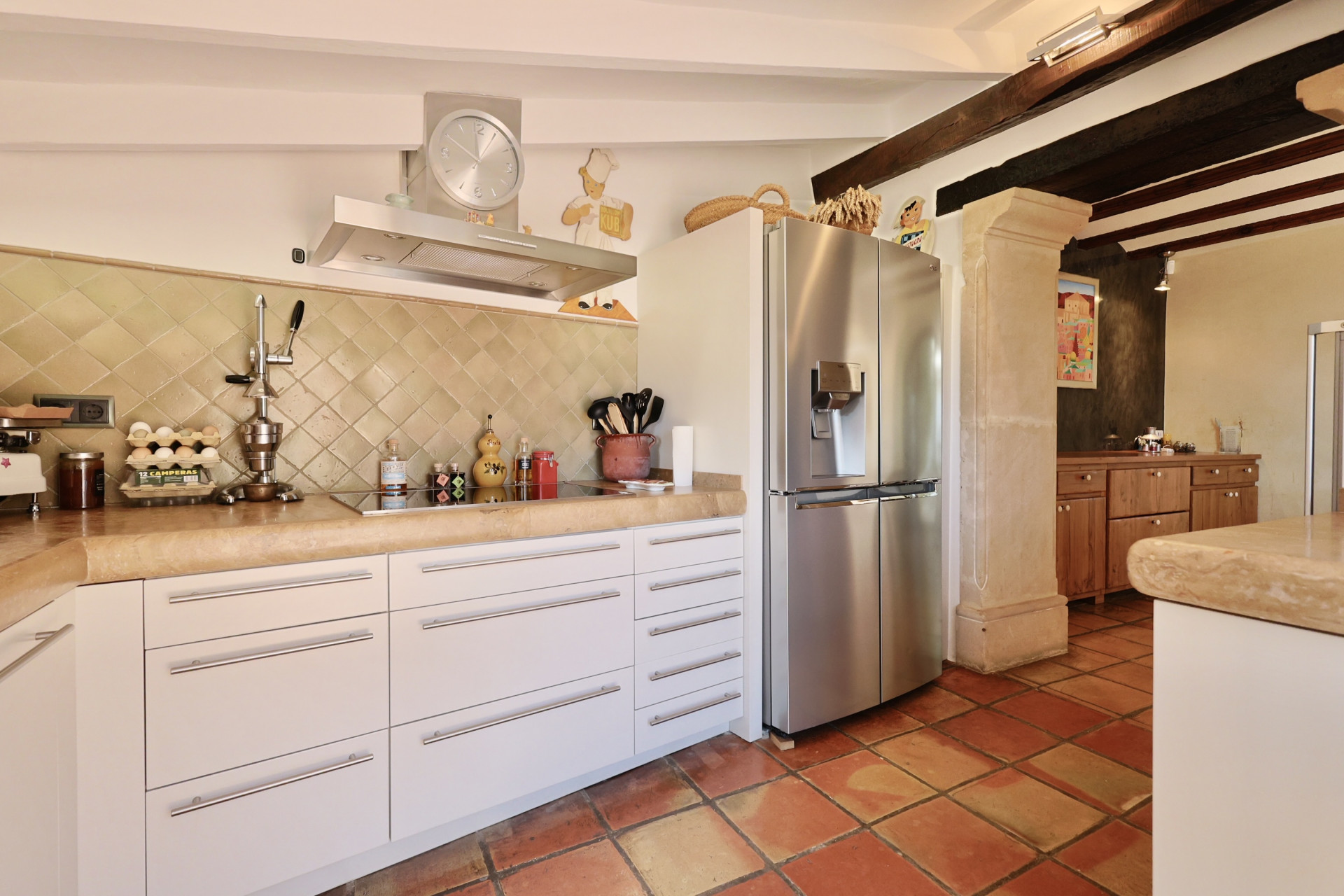 Detalle de la cocina con encimera de piedra, azulejos rústicos y nevera de acero inoxidable.