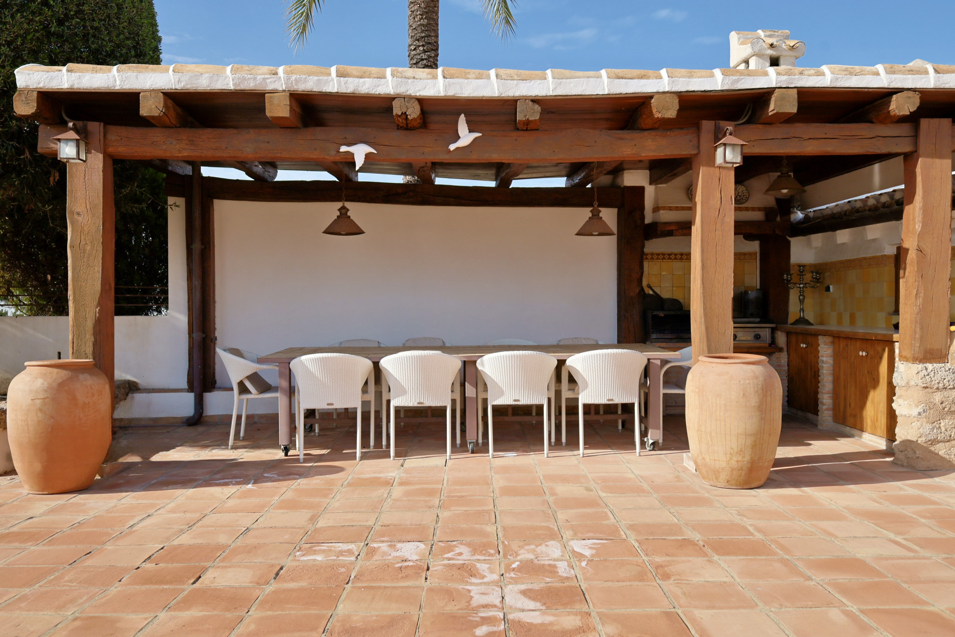 Detalle de la terraza exterior cubierta con mesa de comedor, sillas de mimbre y suelo de terracota.
