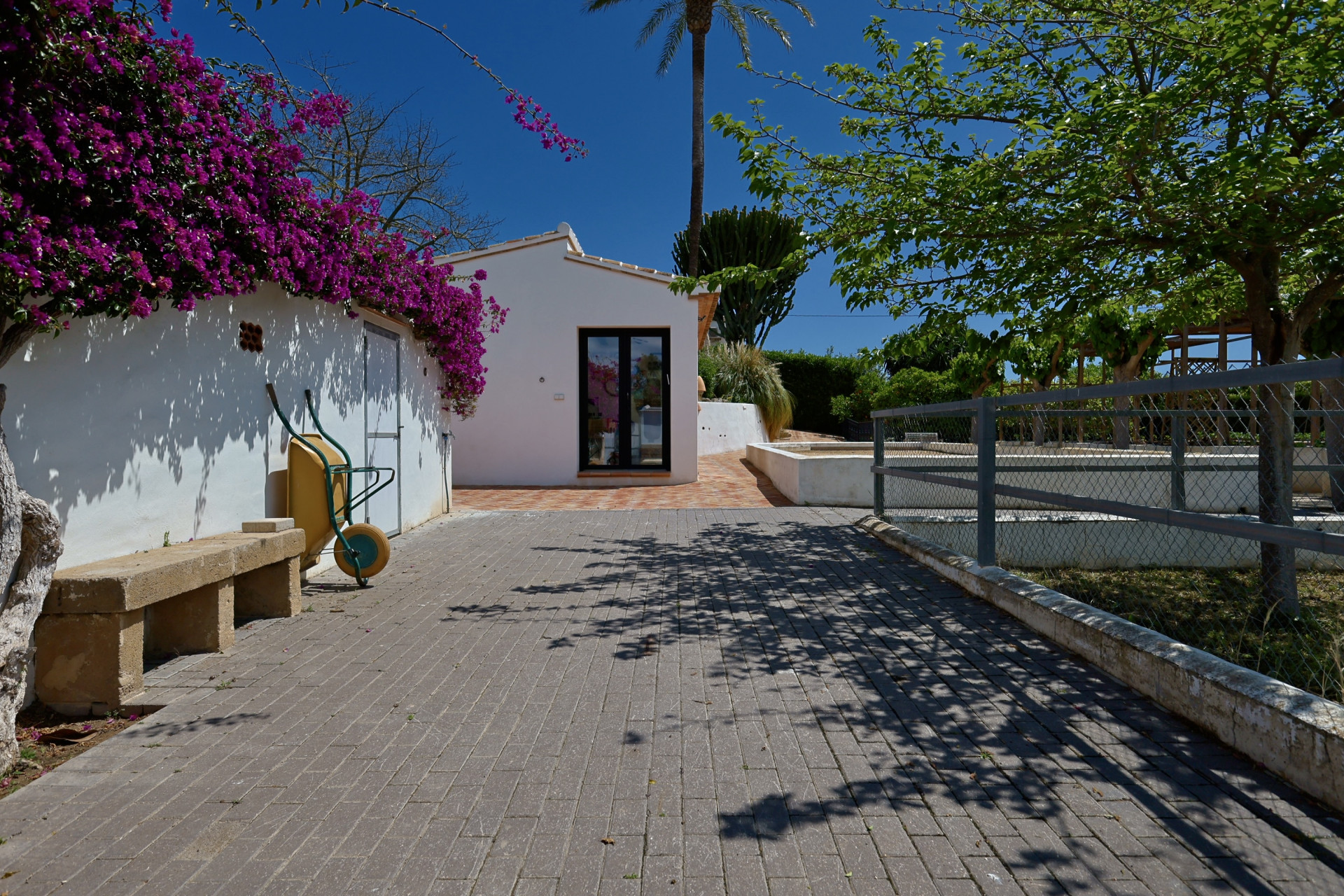 Entrada a la villa con buganvillas y banco de piedra.